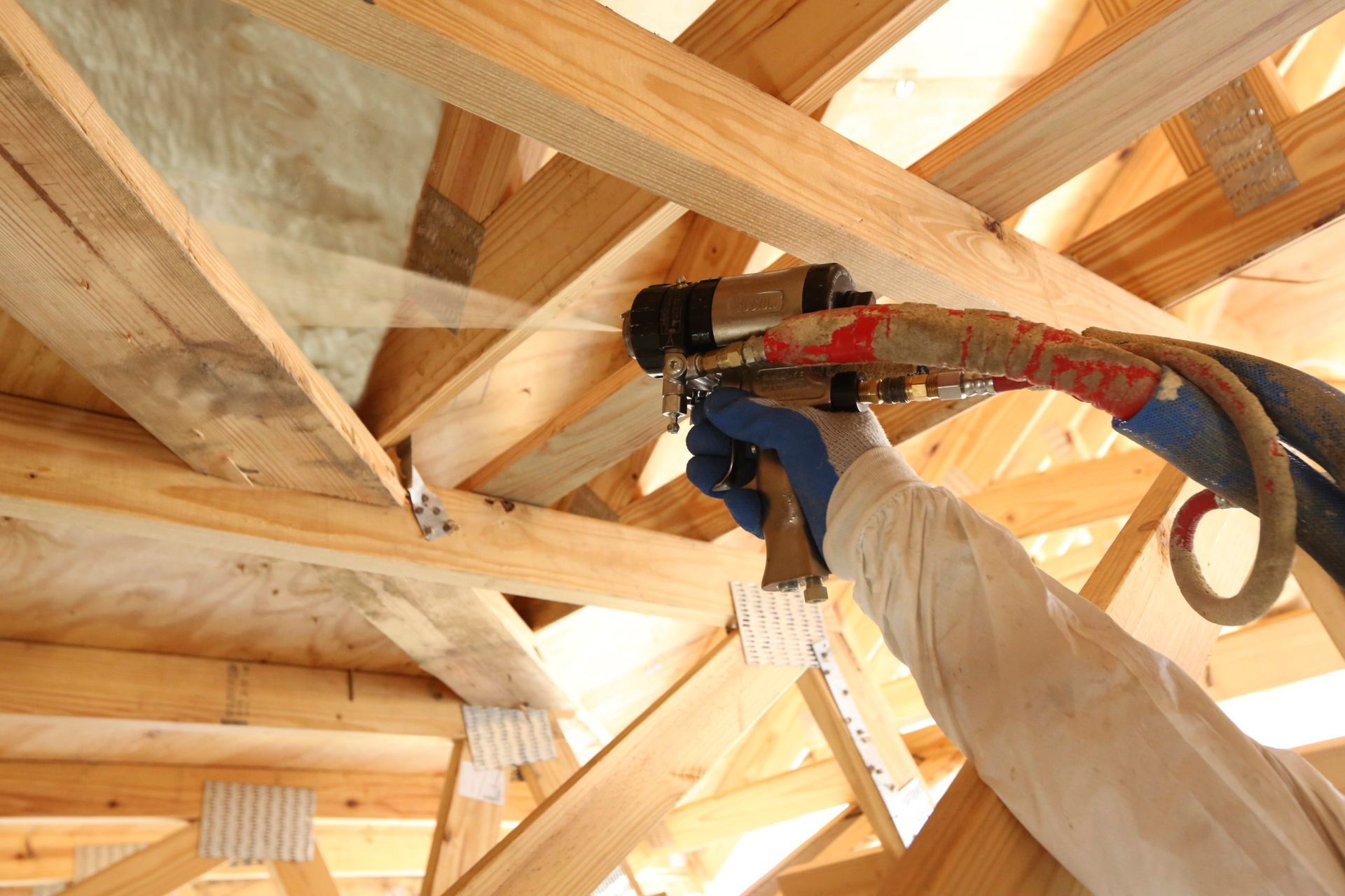 A person is spraying insulation on a wooden structure.